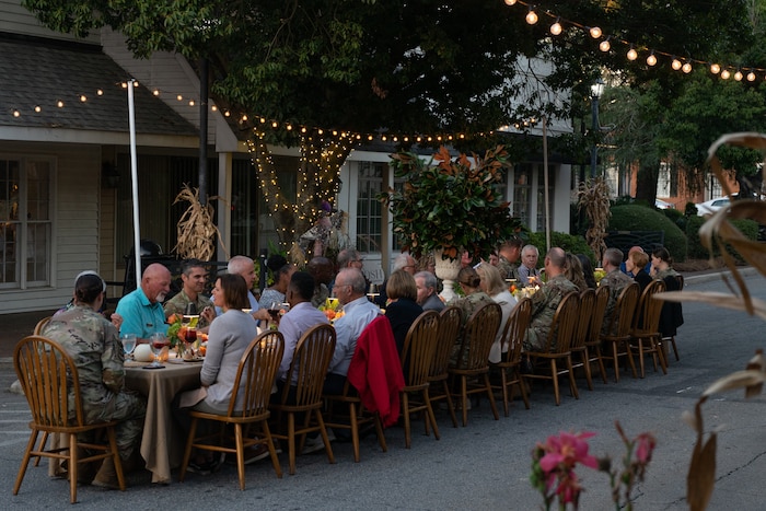 Photo shows group of people dining together at table set up under lights along a street.
