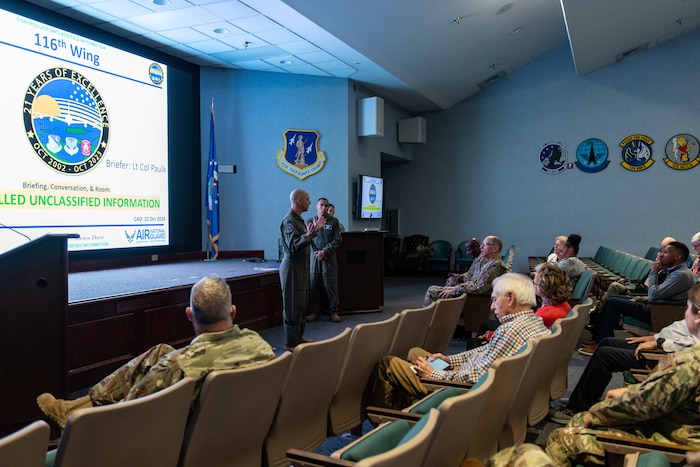 Photo shows man in theater briefing room of people