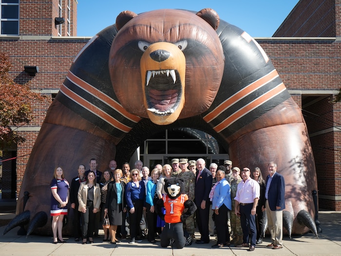 Photo shows group of people standing underneath inflatable arch shaped like a bear
