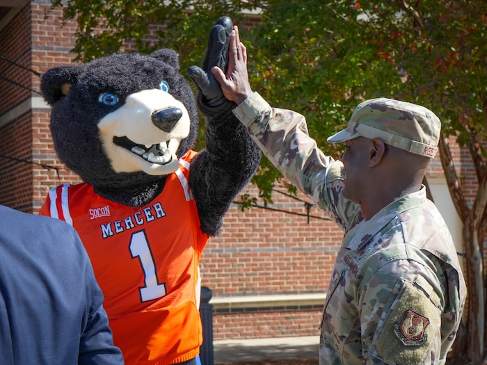 Photo shows man in uniform high-fiving bear mascot