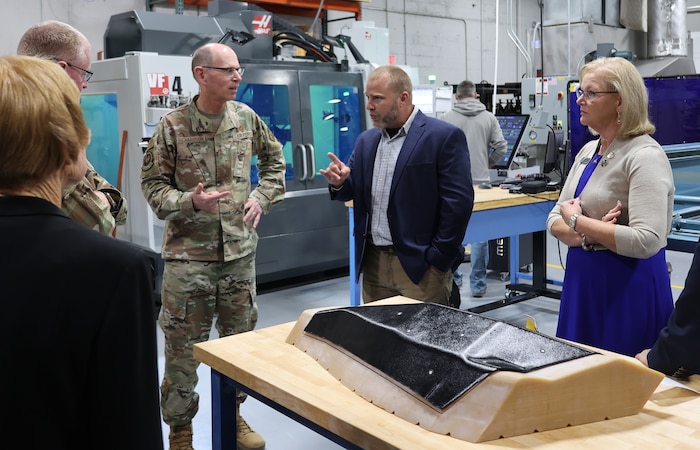 Photo shows group of people talking around equipment on table