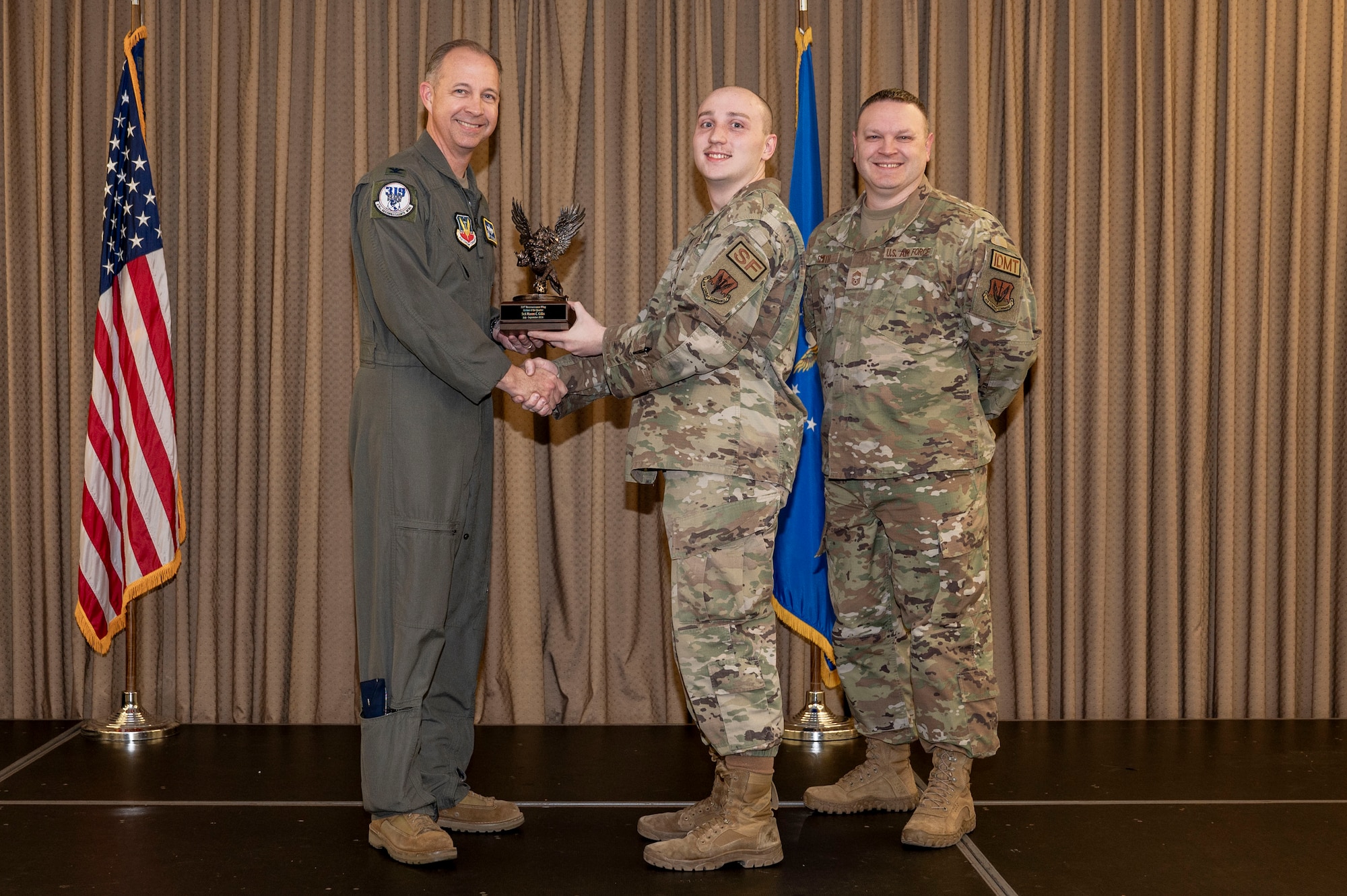 Three military member stand on stage during the awards ceremony while one member receives an award.