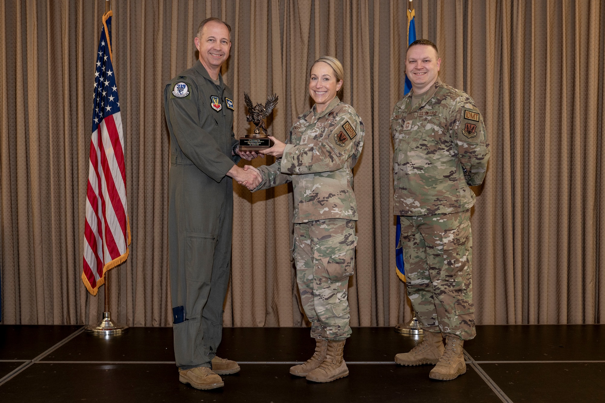 Three military member stand on stage during the awards ceremony while one member receives an award.