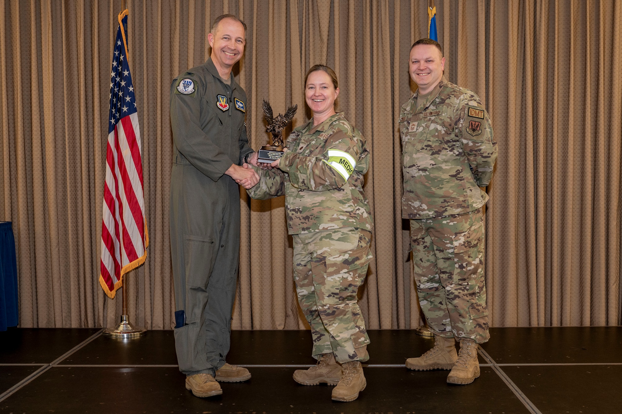 Three military member stand on stage during the awards ceremony while one member receives an award.