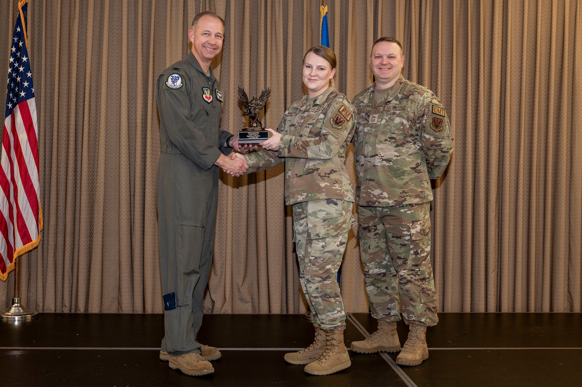 Three military member stand on stage during the awards ceremony while one member receives an award.