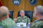 A man sits at a conference table talking to the other participants.