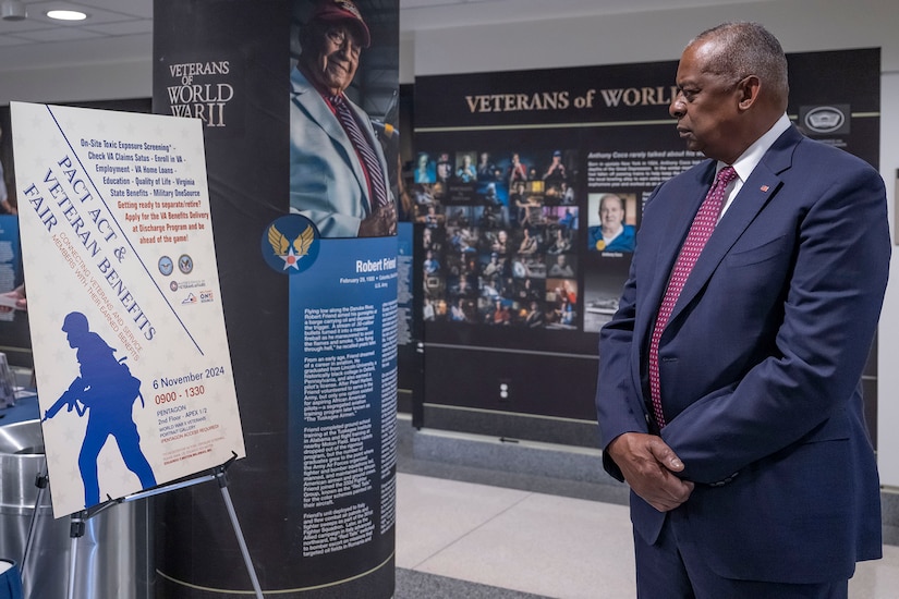 A government official in business attire looks at a poster with information on veterans while in a room with information on the walls.