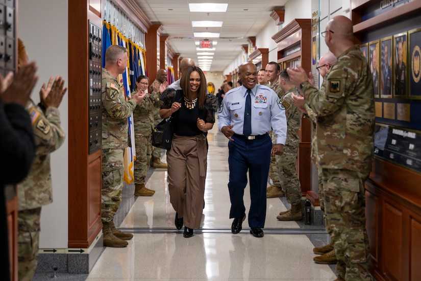 A service member and a civilian woman walks down a hallway flanked by cheering service members.