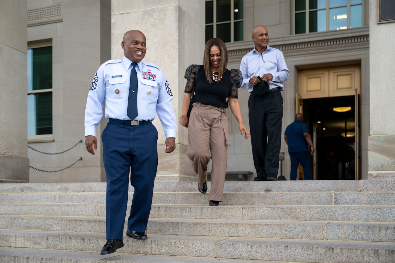 A service member and a civilian woman stands on a staircase.