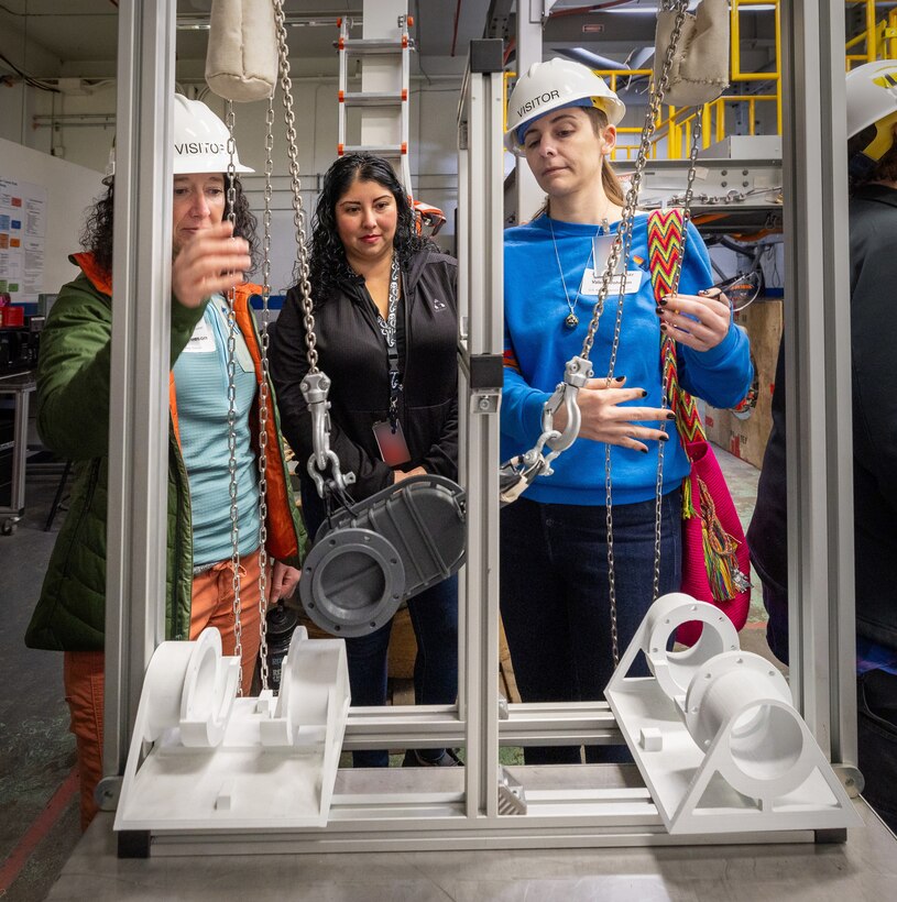 Porsha Molina, continuous training and development supervisor, Code 740, Riggers, helps visiting educators, Megan Bartleson, Olympic High School in Bremerton, and Valerie Johnson, U.S Naval Undersea Museum Keyport, as they try their hand at working a mock up “chainfall” Oct. 21, 2024, during the annual Puget Sound Naval Shipyard & Intermediate Maintenance Facility Educator Day, in Bremerton, Washington. Educators from various academic institutions took part in the day-long learning event. (U.S. Navy photo by Wendy Hallmark)