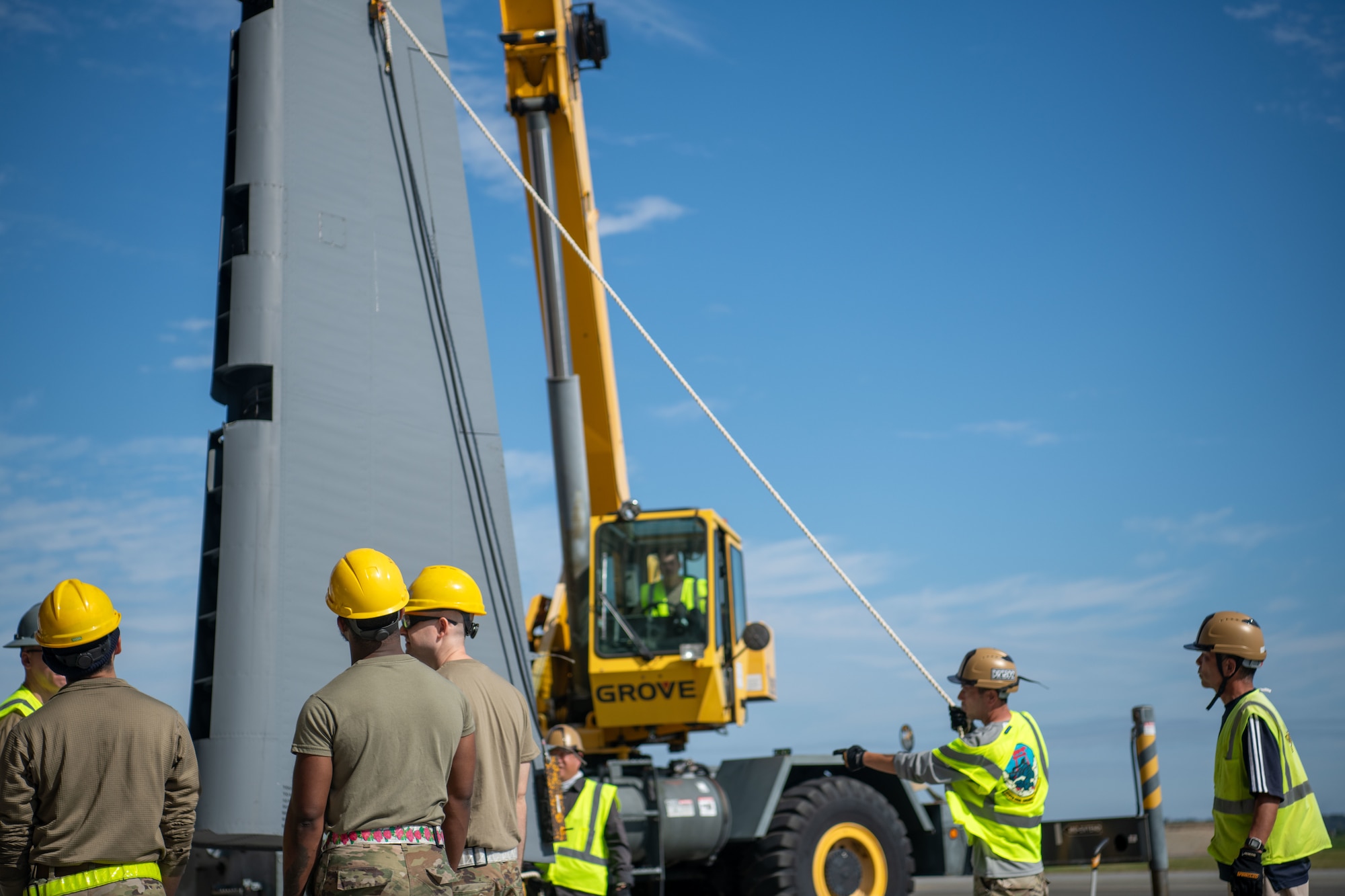 Personnel in construction clothing gather around a yellow crane.