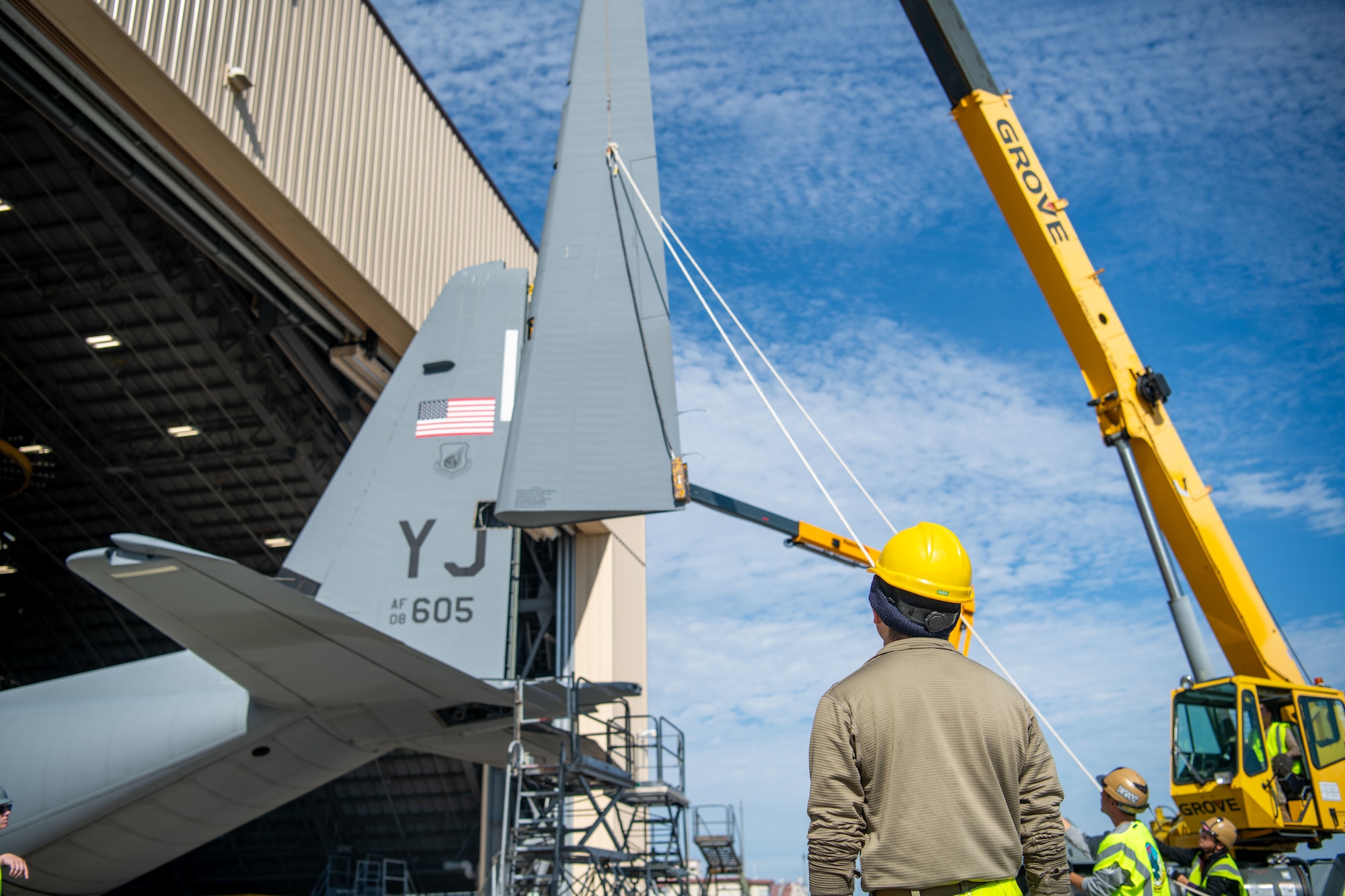 A yellow crane removing a rear fin from an aircraft