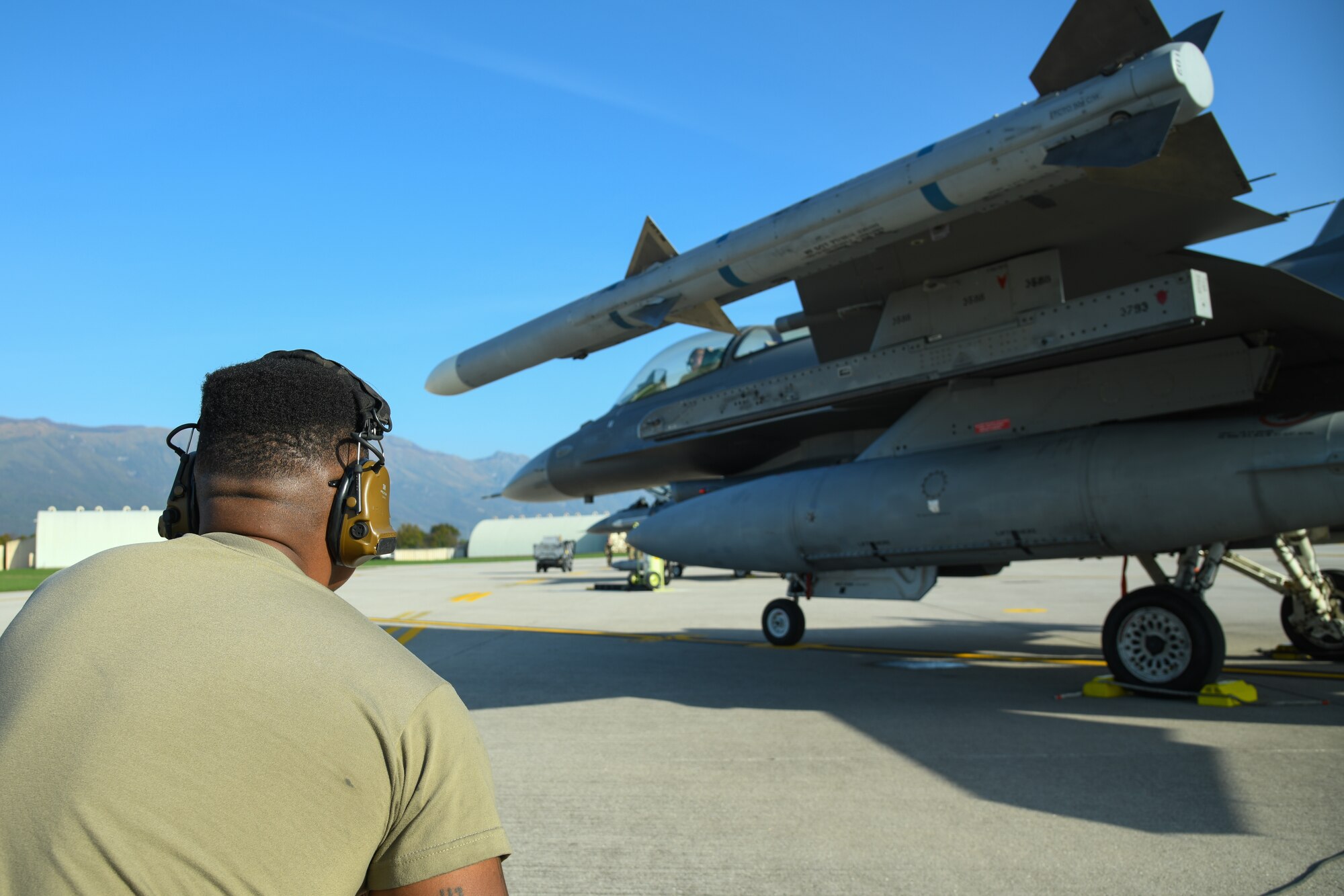 An Airman crouches behind an F-16C fighter jet.