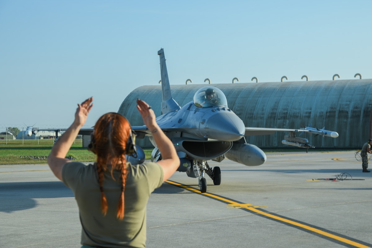 An Airman marshals a fighter jet into place on a flightline.