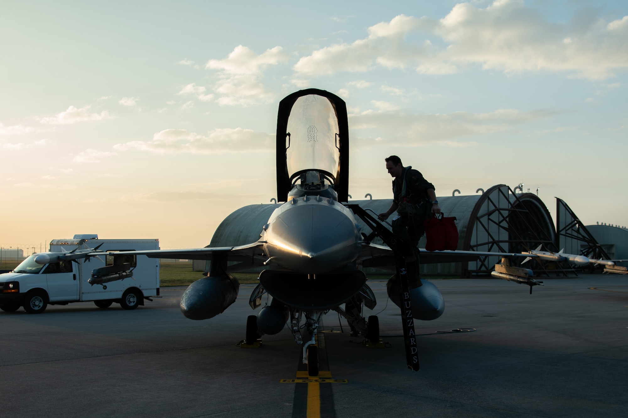A silhouette of an F-16C pilot climbing a ladder into the cockpit of an F-16C fighter jet.