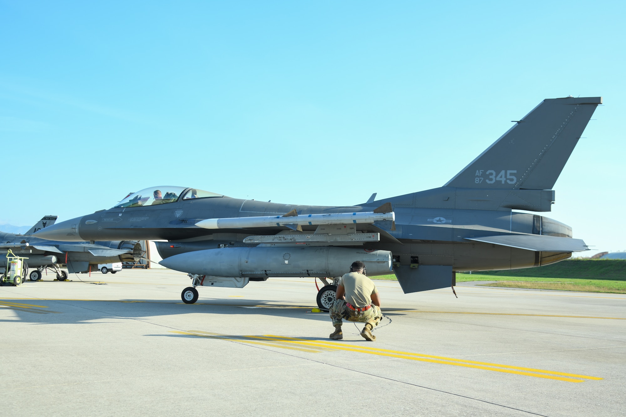 An Airman crouches behind an F-16C fighter jet.