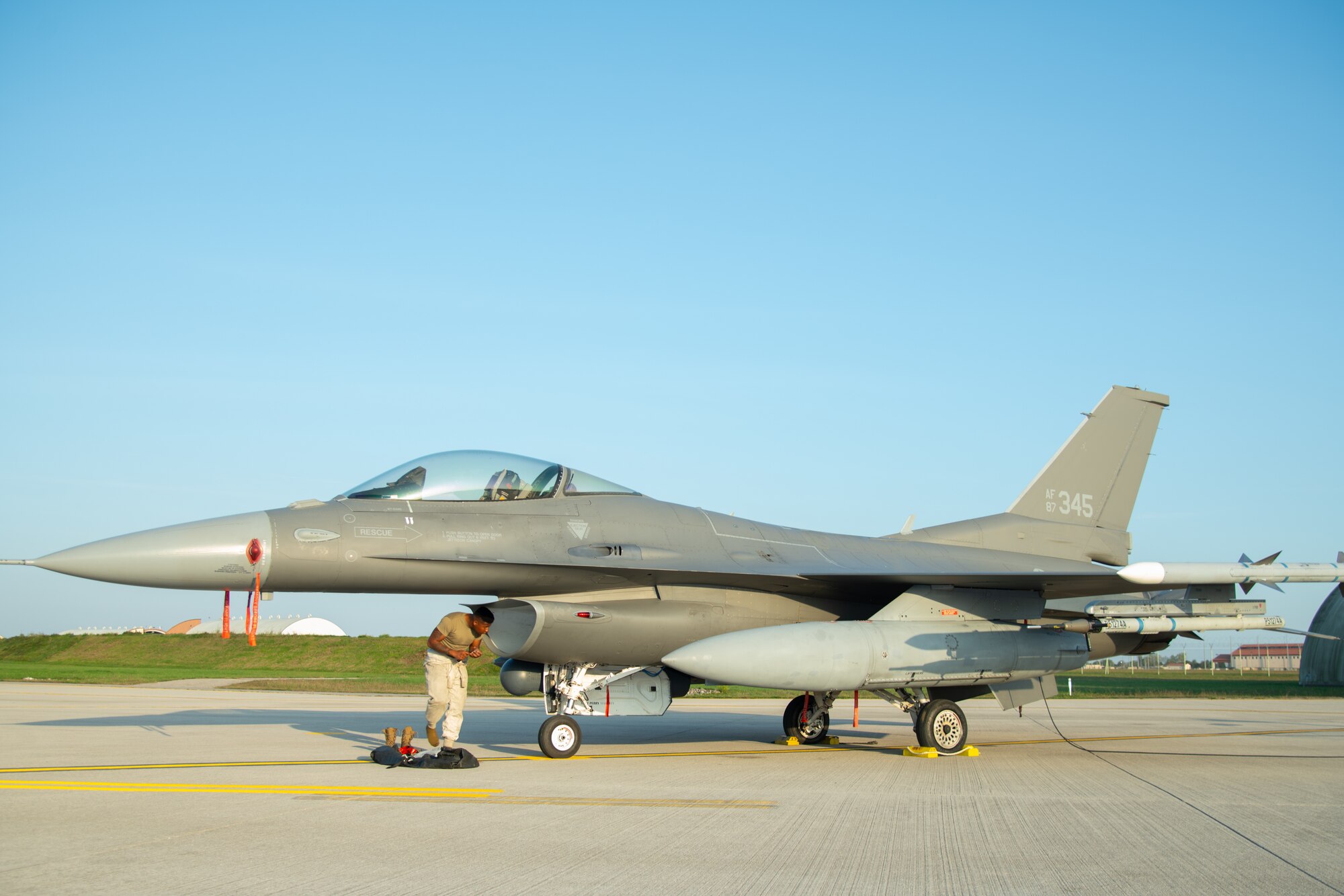 An Airman stands in front an F-16C fighter jet.
