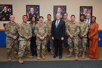 Secretary of the Air Force poses with Airmen in a large room.