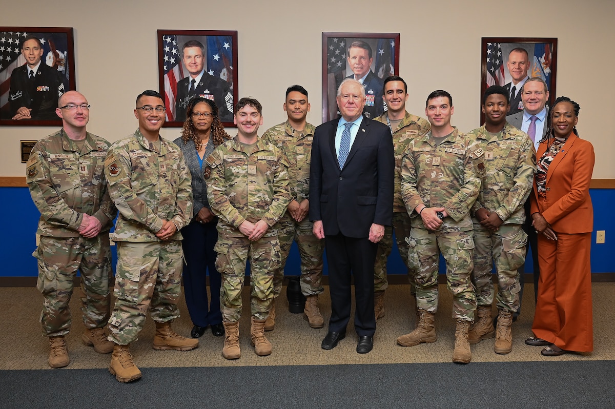 Secretary of the Air Force poses with Airmen in a large room.