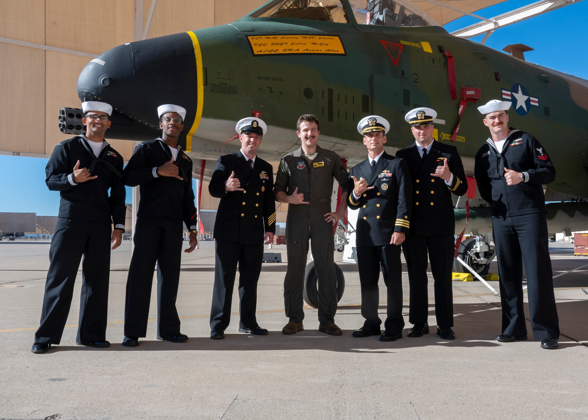 A group of men wearing military dress uniforms and a man in a military flight suit pose for a photo in front of an A-10C Thunderbolt II aircraft.