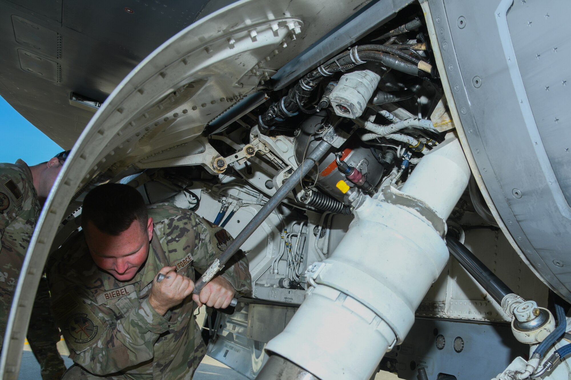 An aircraft mechanic works underneath a F-16C fighter jet.