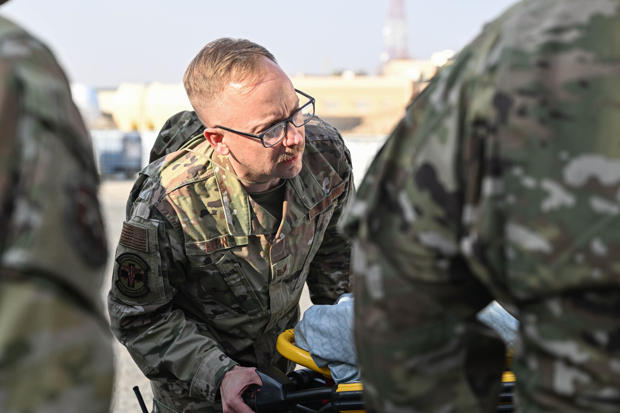 A man in uniform pushes a gurney into an ambulance in front of other men in uniform.