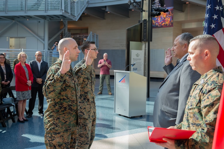 The Secretary of the Navy (SECNAV) Carlos Del Toro, center right, reenlists Cpl. Jack Defilippis, an air traffic control radar technician, center left, and Staff Sgt. Anthony Stevens, a correspondence chief, left, during a visit to the National Museum of the Marine Corps.