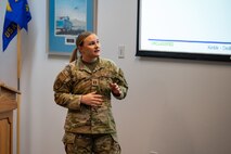 An Airman delivers a presentation and looks towards a screen.
