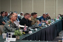 A panel of people sit down at a table for a presentation.