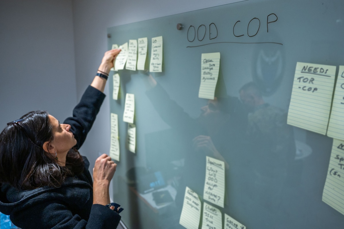 a woman applies sticky notes to a wall during discussion.