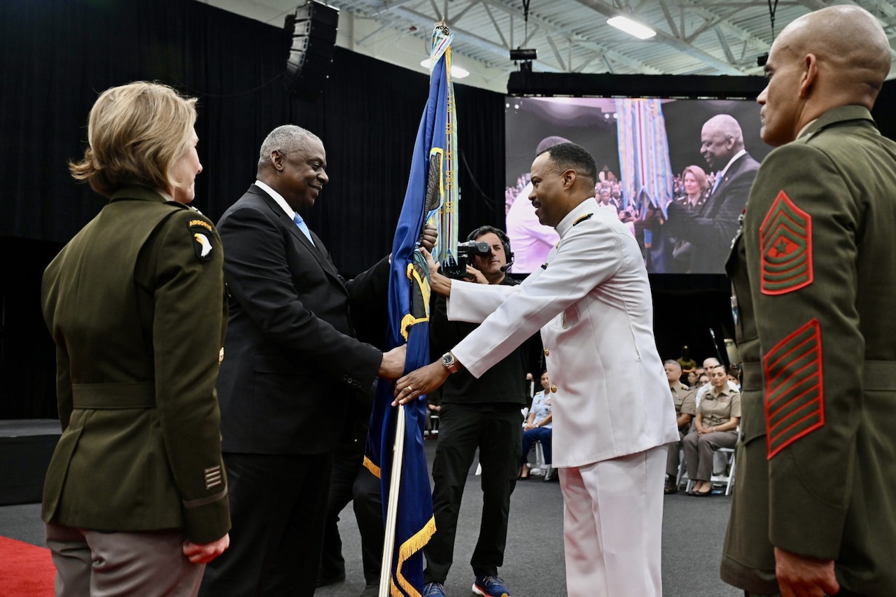 A man hands a flag to a service member in uniform.