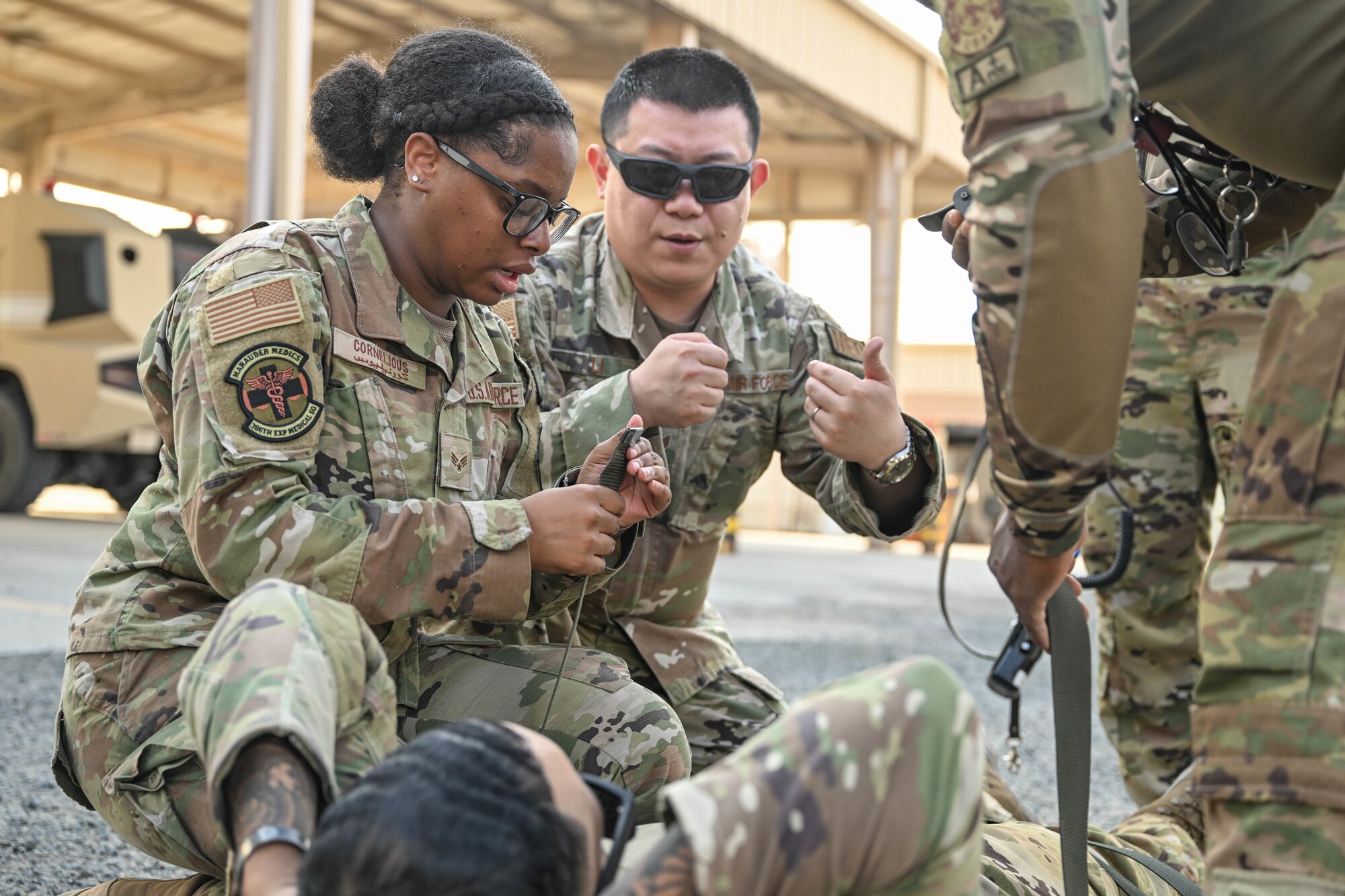 A man in uniform instructs a woman in uniform on how to use the straps on a litter.