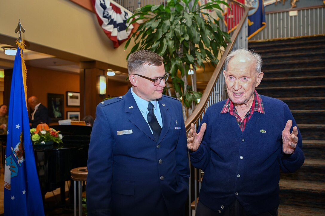 An airman speaks with a veteran at the bottom of the stairs in the lobby of a a building.