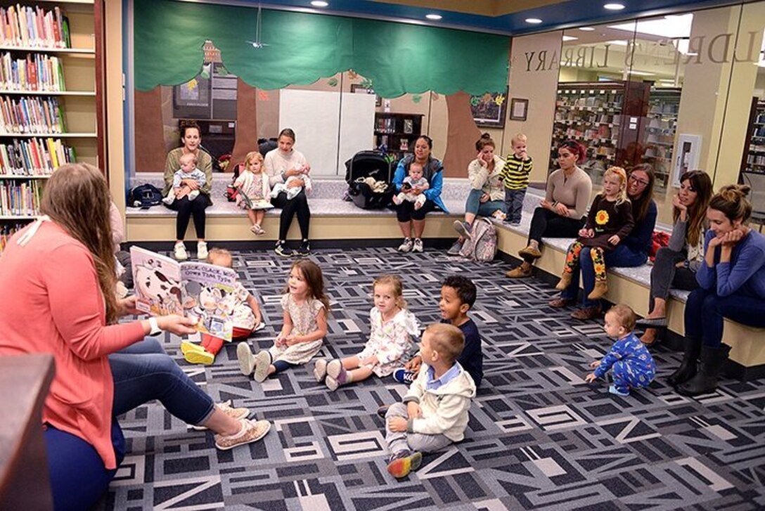 A woman reads a story to children sitting on the floor in a library.