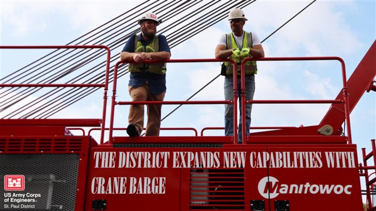 Two people in safety gear standing on a crane barge. The text reads "The district expands new capabilities with crane barge"