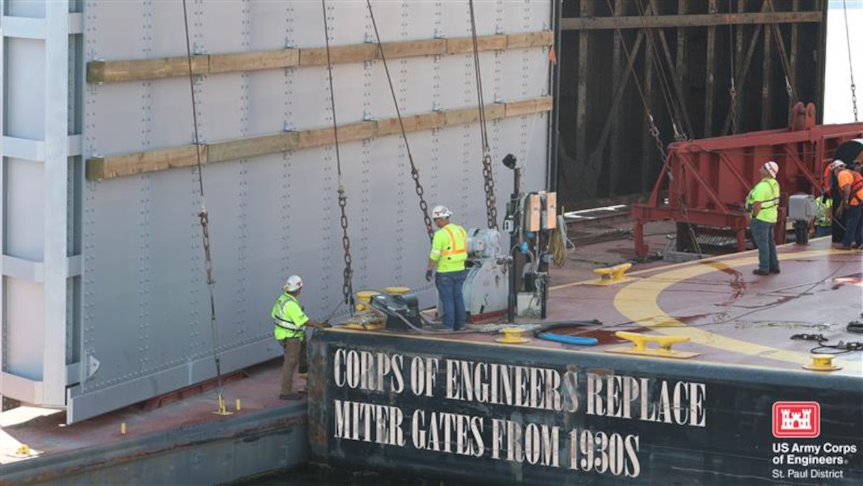 A photo of people in safety gear working on a new miter gate.
Text reads "Corps of Engineers replace miter gates from 1930s"