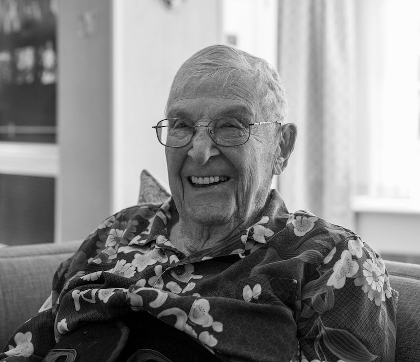 A veteran airman poses for a photo while sitting on a couch indoors.