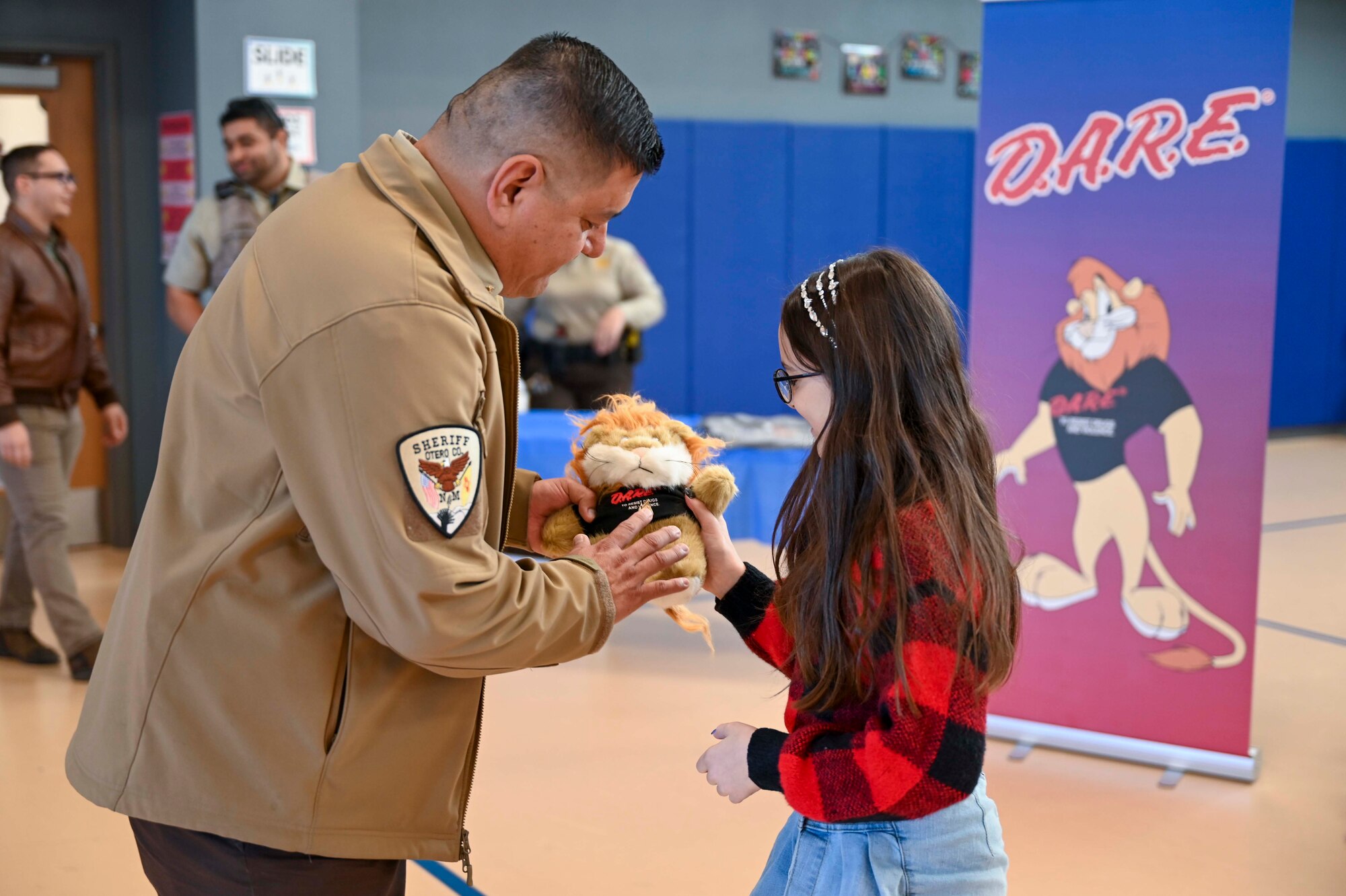 A Drug Abuse Resistance Education graduate receives a teddy bear for producing the best-written essay from Raul Robles, Otero County public relations deputy sheriff, at Holloman Air Force Base, New Mexico, Oct. 31, 2024. The D.A.R.E. program is funded by donations from the community and allows kids to develop and refine their decision-making abilities, empowering them to live safe and healthy lives. (U.S. Air Force photo by Airman 1st Class Michelle Ferrari)