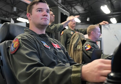 uniformed U.S. Airmen fly MQ-9 simulators