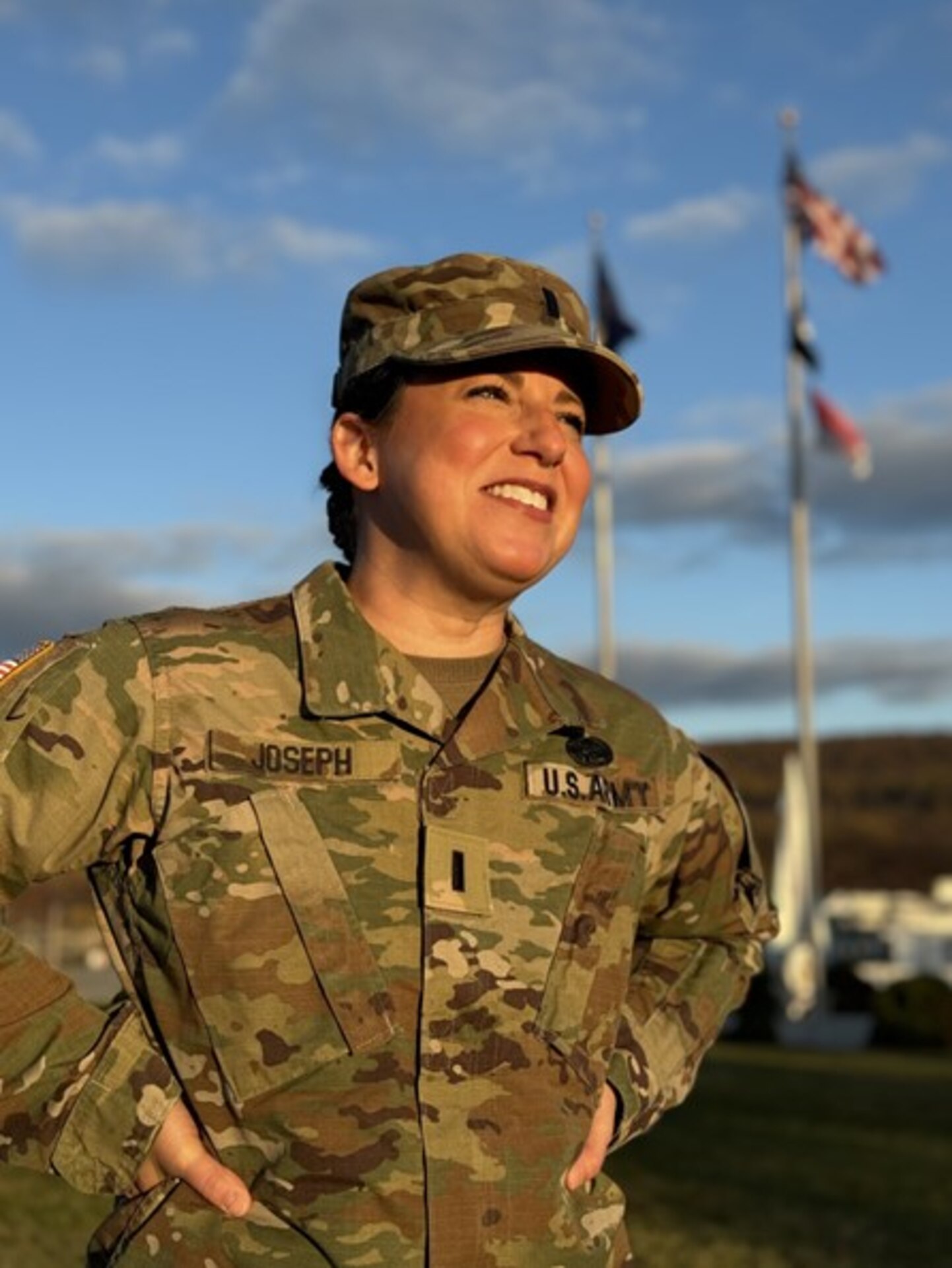 U.S. Army 1st Lt. Sarah M. Joseph, a behavioral health officer with the Medical Readiness Detachment, Joint Force Headquarters, Pennsylvania National Guard, smiles under Pennsylvania and American flags at Fort Indiantown Gap, Pennsylvania, Nov. 2, 2024. Joseph recently commissioned after a five-year break in service. (U.S. Army National Guard photo by 1st Sgt. HollyAnn Nicom)
