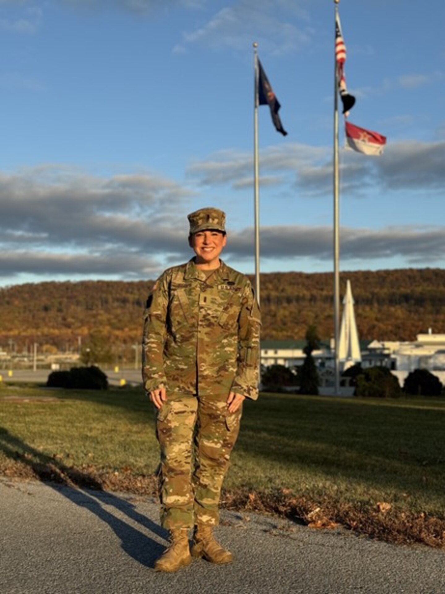 U.S. Army 1st Lt. Sarah M. Joseph, a behavioral health officer with the Medical Readiness Detachment, Joint Force Headquarters, Pennsylvania National Guard, smiles under Pennsylvania and American flags at Fort Indiantown Gap, Pennsylvania, Nov. 2, 2024. Joseph recently commissioned after a five-year break in service. (U.S. Army National Guard photo by 1st Sgt. HollyAnn Nicom)