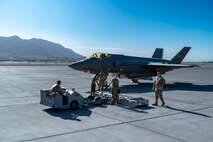 Airmen lift a munition onto a lift truck in front of an F-35A Lightning II.