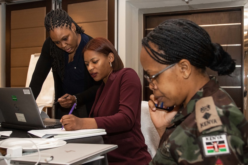 A group of female service members work around a desk in a room.