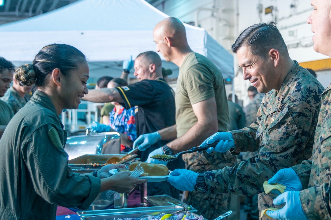 U.S. Navy Lt. Fredy Villamil, right, the command chaplain assigned to Marine Medium Tiltrotor Squadron (VMM) 165 (Reinforced), 15th Marine Expeditionary Unit, and a native of California, serves food to Hospital Corpsman 2nd Class Marianne Greene, also assigned to VMM-165 (Rein.), 15th MEU, during a steel beach event aboard the amphibious assault ship USS Boxer (LHD 4) in the Pacific Ocean Nov. 10, 2024. The steel beach was held on the second day of the 15th MEU’s 249th Marine Corps birthday celebrations as Boxer transited past the international dateline. Elements of the 15th MEU are currently embarked aboard Boxer and are conducting routine operations in U.S. 3rd Fleet. (U.S. Marine Corps photo by Sgt. Amelia Kang)