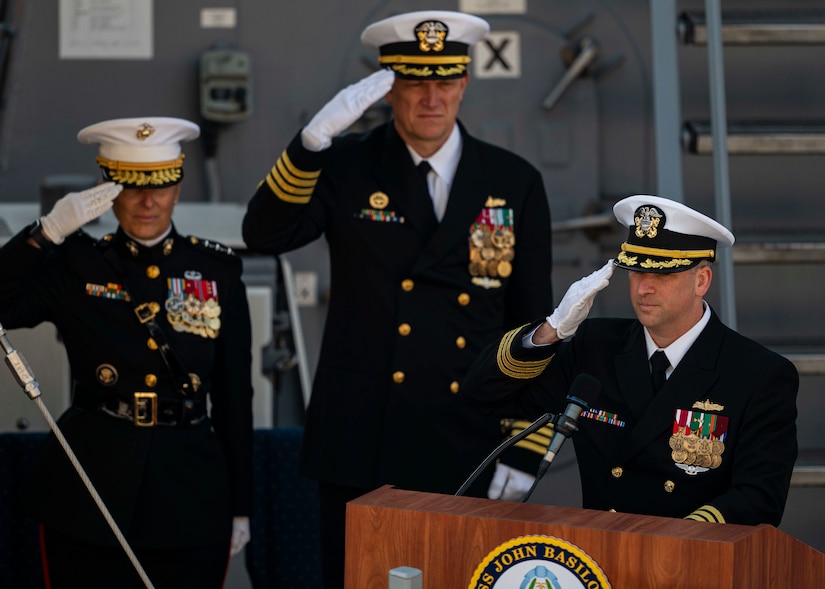 Three high-ranking sailors salute in front of a podium.