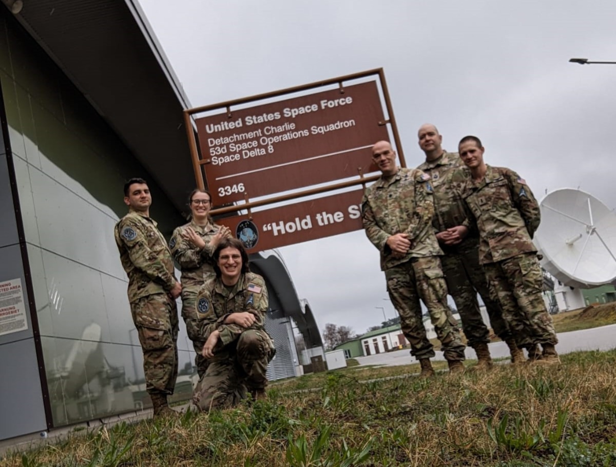 Uniformed members stand in front of a sign in Germany during a TDY.