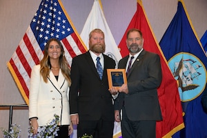 One woman and two men standing in front of flags