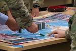 Participants point to game pieces on a board game designed to simulate air combat scenarios.