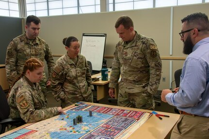 Airmen standing around a table overlooking a board game simulating an agile combat scenario.