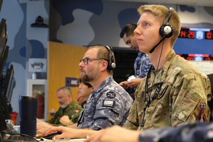 uniformed military members work at computers while wearing headsets